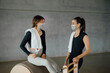 © BASILICOSTUDIO STOCK - Women wearing face masks and sport clothing, talking and having a break between fitness classes in a big industrial gym, loft center. Fitness, well being in a health club.