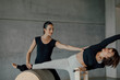 © BASILICOSTUDIO STOCK - Young fit woman is concentrated on exercising on pilates barrel with female instructor at gym. Sports equipment. Active and healthy lifestyle rehabilitation concept.
