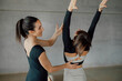 © BASILICOSTUDIO STOCK - Portrait of Beautiful brunette female instructor helping a woman to practice Pilates stretching exercise during personal fitness lessons in a gymnasium. Coaching in health club during daytime.