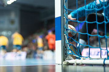 Detail of handball goal post with net and handball match in the background.