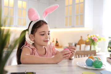 Poster - Cute little girl in bunny ears headband painting Easter eggs at table indoors