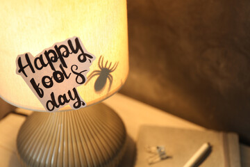 Wall Mural - Glowing lamp with spider and words Happy Fool's Day on nightstand. Space for text