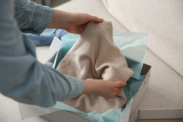 Woman taking soft cashmere sweater out of box indoors, closeup
