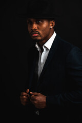 Portrait of attractive, cute, stylish professional African American businessman in stylish suit, white shirt and black hat, isolated on dark background. Low key. Selective focus