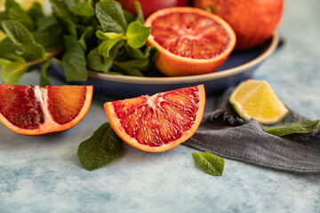 Wall Mural - Red Sicilian oranges with limes and mint on blue background. Whole and sliced citrus.