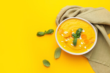 Bowl of tasty carrot cream soup on color background