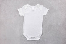 White Baby Girl Or Boy Bodysuit Mockup On The Gray Concrete Background. Design Onesie Template, Print Presentation Mock Up. Top View. Flat Lay.