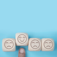 Wall Mural - world mental health day concept or feedback rating and positive customer review, Businessman hand choose smile face, wood cube with happiness and sadness face icon on blue background