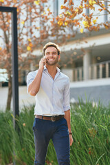 Wall Mural - Smiling businessman talking on his phone while walking outside