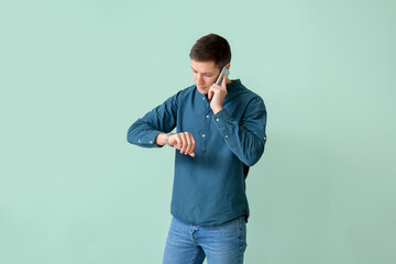 Handsome young man talking by mobile phone on color background