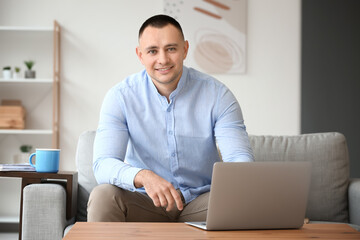 handsome young man with laptop sitting on sofa at home