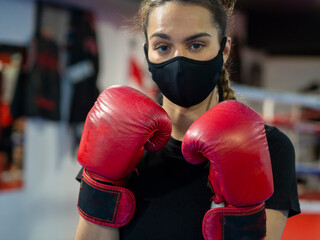 Boxer girl wearing a mask and red boxing gloves in a gym. Fighting covid and virus concept. Woman training with a mask, the new normal.