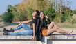 © maemodnit13 - Happiness two young women laughing and holding hand each other while sitting back and back outdoors. Cheerful Best friends or sisters feeling. Love between same-sex couples, family and friend concept