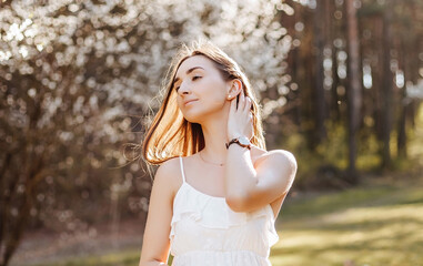 Girl with flowers in the spring in the park. Brunette with long hair on a background of summer nature. Youth and beauty.