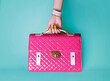 Woman hand with yellow manicured nails holding pink purse on blue background. 
