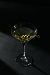 Glass of classic dry martini cocktail with olives on dark stone table against black background.