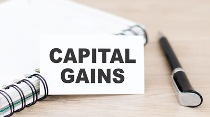 Text Capital Gains on a white card next to a notebook and a black pen on the table