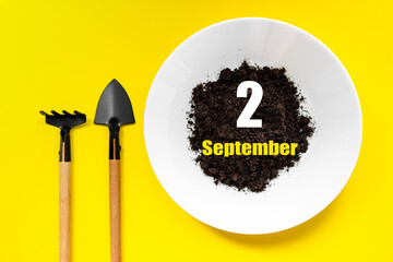 September 2nd. Day 2 of month, Calendar date.White plate of soil with a small spatula and rake on yellow background. Autumn month, day of the year concept.