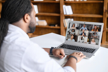 Wall Mural - Back view on the laptop screen with many profiles on it, an African-American guy is using computer app for video meeting, online conference with coworkers, colleagues, virtual briefing