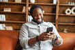 © Vadim Pastuh - Cheerful African-American guy enjoys messaging on the smartphone sitting on the couch, a guy typing on the phone, chatting online, smiles