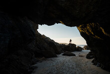 Silhouette Of Man Standing On Top Of Rocks At Entrance Of Empty Beach Cave, Asturias, Spain