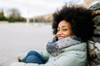 © Xavier Lorenzo/Westend61 - Smiling young woman in warm clothing while sitting outdoors