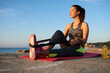 © Guille Faingold/Stocksy - Sportswoman stretching leg with straps on mat at sea