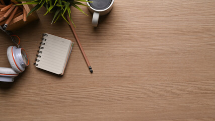 Fototapete - Top view of office desk with coffee cup, headphone, plant, notebook and copy space on wooden background.