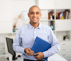 Smiling manager in office standing near workplace. Light tone photo