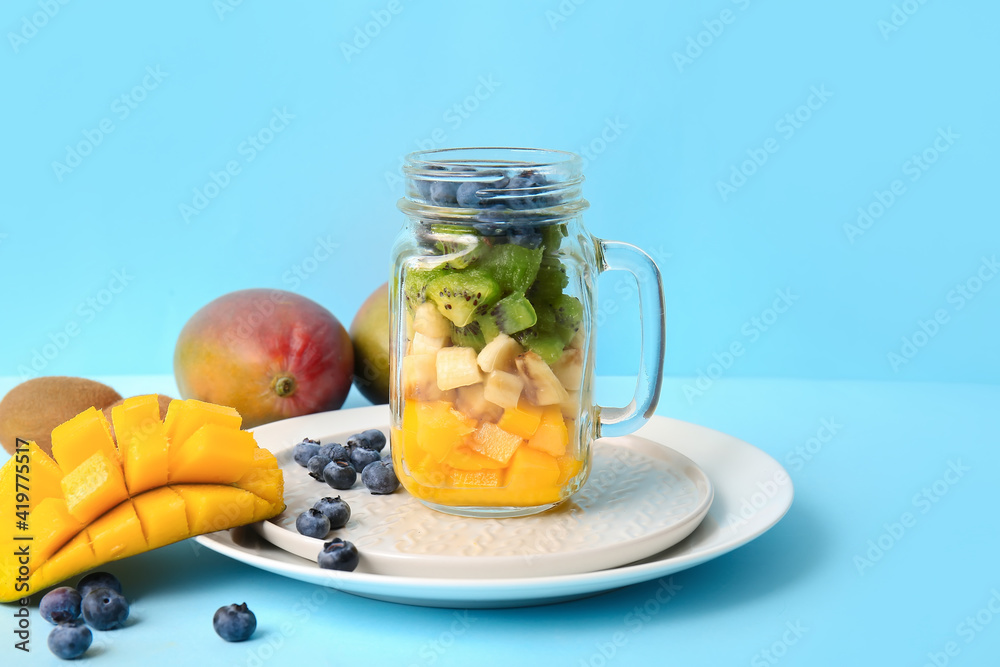 Mason jar with tropical fruit salad on color background