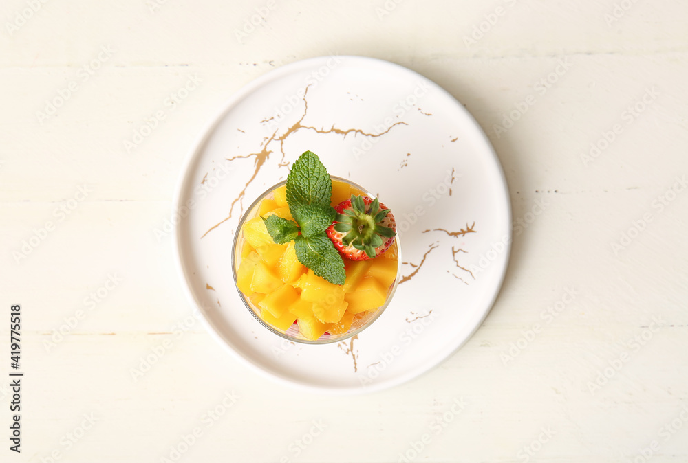 Glass with tropical fruit salad on light wooden background
