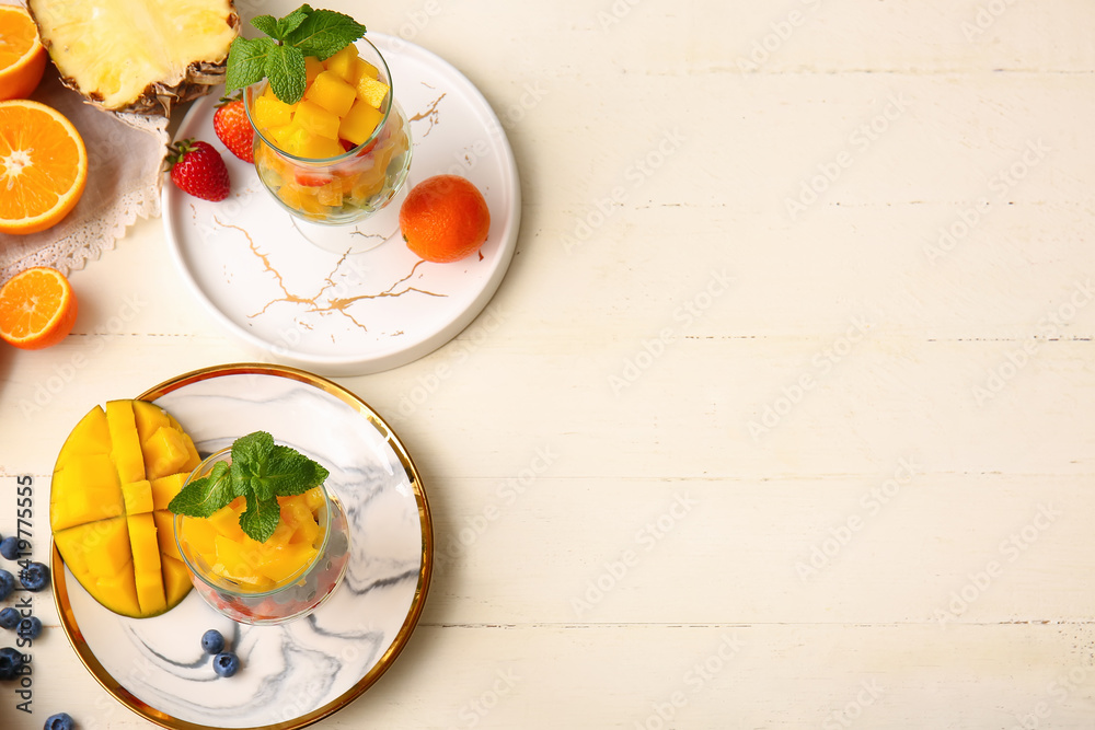 Glasses with tropical fruit salad on light wooden background