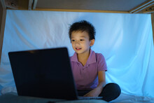 Asian Boy Child To Make A Camp To Play Imaginatively Watching A Film On Laptop In The Darkness Of The Camp In Living Room At Home.
