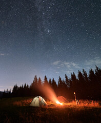 Wall Mural - hiker standing near campfire under night starry sky.