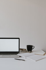 Wall Mural - Minimalist home office desk workspace. Laptop with blank copy space mockup on table with coffee cup, paper sheet, stationery against white wall. Work, business background.