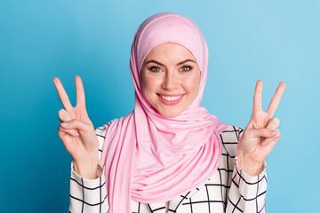 Wall Mural - Close-up portrait of lovely cheerful glad muslimah girl showing double v-sign isolated over shine blue color background