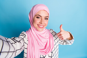 Wall Mural - Self-portrait of pretty cheerful glad muslimah girl showing thumbup advert advice isolated over bright blue color background