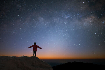 Silhouette of young traveler and backpacker watched the star and milky way alone on top of the mountain. He enjoyed traveling and was successful when he reached the summit.