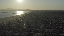 Aerial: Low City Stretches Into Distance Along Wide Sandy Beach Under Hazy Golden Sunshine