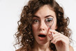 Half-naked curly woman expressing surprise while using eyelash curler