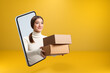 © Olga - A smiling beautiful girl got out of her smartphone and hands over boxes with orders. Young woman with online shopping on the mobile phone screen. Copy space.