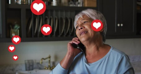 Sticker - Multiple heart icons floating against african american senior woman talking on smartphone