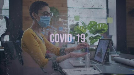 Poster - Covid-19 text and grunge effect against woman wearing face mask sanitizing her hands at office