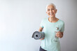 © Dragana Gordic - Woman with yoga mat while standing in fitness studio. Woman With Rolled Up Exercise Mat In Gym. Portrait of confident mature woman with exercise mat smiling in gym