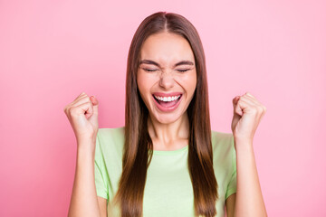 Poster - Photo of impressed lucky young lady wear green t-shirt rising fists closed eyes isolated pastel pink color background