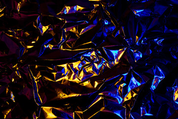 Abstract yellow and blue aluminum wrinkled foil background texture reflecting red and blue light