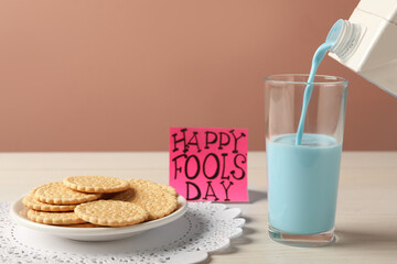 Wall Mural - Pouring light blue milk into glass, cookies and words Happy Fool's Day on table