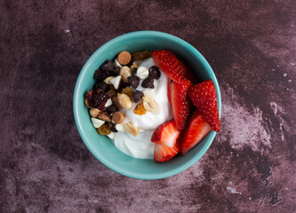 Wall Mural - Overhead view of a bowl with plain Greek yogurt and a candy trail mix and strawberries on a marron tabletop illuminated with natural light.