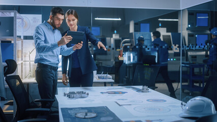 Wall Mural - Factory Office Meeting Room: Male Chief Engineer Holds Digital Tablet Computer, Shows Screen to Female Project Manager, They Talk, Find Optimization Solution. Modern Industry 4.0 CNC Machinery