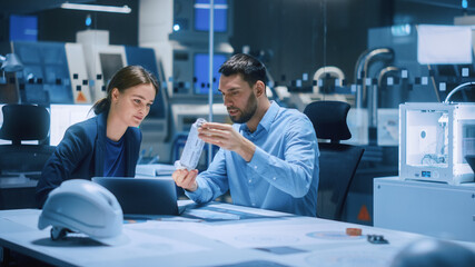 Poster - Industry 4.0 Modern Factory Meeting Room: Chief Engineer Holds Mechanism, Shows it to Female Designer, Use Laptop. Scientists in Contemporary Lab Build Electronic Machinery for With Futuristic Design